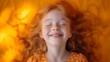 Cheerful redhaired girl smiling while laying on orange bed sheet in cozy and bright bedroom