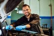 © bnenin - A portrait of a mechanic man smiling for the camera while working on a car, using some tools.