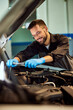 © bnenin - A smiling mechanic is using some tools at his car repair service, working.