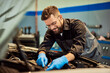 © bnenin - A smiling mechanic fixing a car, holding some cables in the opened hood.