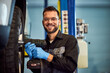 © bnenin - Portrait of a smiling mechanic, using a drill, screwing the wheel, and working in his garage.