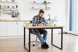 © sofiko14 - Full length of attractive Caucasian businessman sitting at office desk with digital devices in spacious dining room. Self-employed worker carrying out professional activity in comfortable workplace.