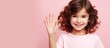 a little girl is waving her hand in front of a pink background . High quality