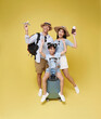 Happy fun asian family vacation portrait. Father, mother and daughters ready for travel flight with suitcase isolated on yellow studio background.