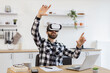 © sofiko14 - Caucasian technology manager satisfied with new modern gadget. Joyful bearded man wearing VR headset and gesturing from happiness while working distance at kitchen.