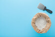 Spatula and opened paper bag of white dry finishing putty for plastering ceiling and wall surfaces on pastel blue table background. Repair work of home. Closeup. Empty place for text. Top down view.