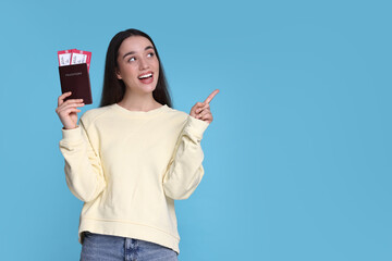 Canvas Print - Happy woman with passport and tickets pointing at something on light blue background. Space for text