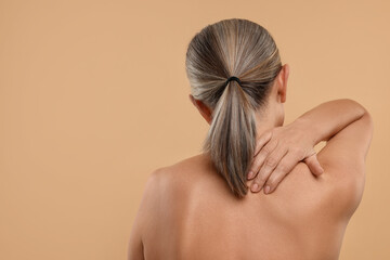 Poster - Mature woman suffering from pain in her neck on beige background, back view. Space for text