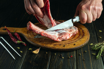 Wall Mural - Chef uses a knife to remove meat from bones on a cutting board before preparing a dinner or barbecue. Low key concept of the process of cooking meat on a kitchen table by the hands of a butcher.