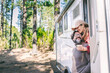 © simona - Happy people on travel lifestyle sitting on the door of a camper van parking in the nature forest park. Enjoying vanlife couple. Renting vehicle for vacation and off grid independent house motorhome