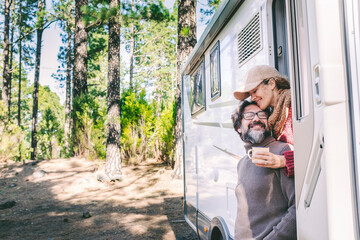 Wall Mural - Happy people on travel lifestyle sitting on the door of a camper van parking in the nature forest park. Enjoying vanlife couple. Renting vehicle for vacation and off grid independent house motorhome