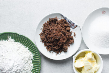 overhead view of mise en place for sugar cookies dough, ingredients for chocolate chip cookies on a marble countertop, top view of butter sugar brown sugar and flour on a white background