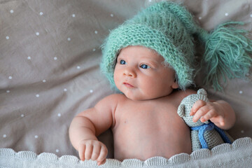 Sticker - Cute newborn baby in warm hat with toy lying on bed, top view