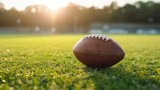 Fototapeta Sport - An American football ball lies on the green turf of a football field at sunset. Team ball game, sport, rugby, football stadium