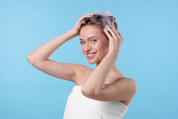 Poster - Happy young woman washing her hair with shampoo on light blue background