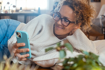 Cheerful woman browsing on the phone at home laying on the floor in indoor online social media leisure activity. People use mobile cellular and internet connection. Happy lifestyle modern female house