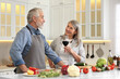 © New Africa - Happy senior couple cooking together in kitchen. Woman with glass of wine near her husband