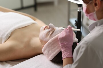 Poster - Cosmetologist applying mask on woman's face in clinic, closeup