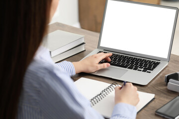 Wall Mural - E-learning. Woman taking notes during online lesson at table indoors, closeup