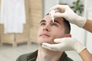 Sticker - Doctor applying medical drops into young man's eye indoors