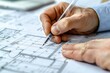 © romanets_v - a person's hand holding a pen, poised over architectural or technical drawings, suggesting work on a design or planning project
