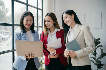 Poster - Three women are standing in a room, smiling and holding a laptop