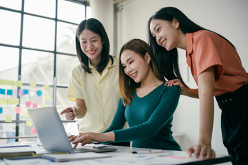 Poster - Three women are sitting at a table looking at a laptop