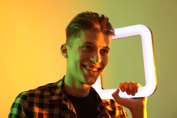 Poster - Young man with square lamp on color background in neon lights