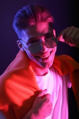 Poster - Stylish young man in sunglasses on dark background in neon lights