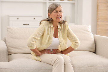 Poster - Menopause. Woman suffering from abdominal pain on sofa at home