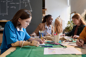 Side view portrait of teenage girl with prosthetic hand drawing clothing sketches in tailoring class