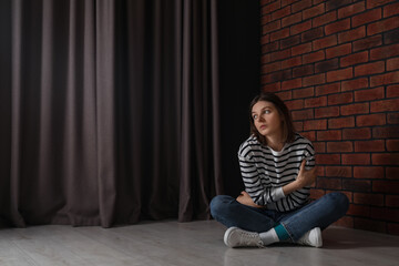 Canvas Print - Sad young woman sitting on floor indoors, space for text