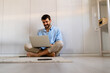 Male sitting on floor uses Internet, writes project report. Productive distant worker from home.