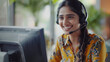 Happy Indian call center agent wearing headset talking to client working in customer support office. Professional contract service telemarketing operator using laptop having conversation. Candid shot 