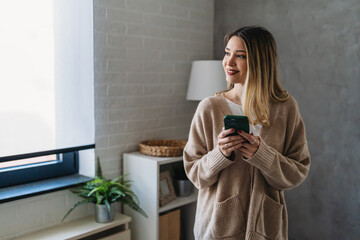 Wall Mural - Smiling young woman chatting in social networks, working, using mobile applications at home.