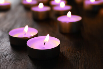 Wall Mural - Beautiful burning violet candles on wooden table, closeup. Funeral attributes