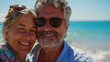 Close up portrait of retired family couple relaxing on the beach, taking selfie. Beautiful middle aged or senior loving couple enjoying life. Retirement holiday, adventure and romantic trip in nature
