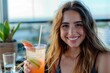 Cheerful young lady with a sparkling smile holding a colorful drink in a casual outdoor setting
