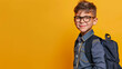 Close-up portrait of smiling pre-teen boy with glasses and school bag or backpack isolated on yellow studio background, copy space for text