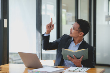 Wall Mural - A man in a suit is pointing at a book on a desk