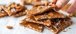 Close up of hand breaking peanut brittle with crunchy texture and peanuts on bright white background