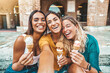 © Davide Angelini - Happy group of women eating ice cream cones walking on city street