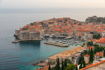 Wall Mural - Aerial view of Dubrovnik Old town with turquoise water harbor on Adriatic sea at sunset, Dalmatia, Croatia. Medieval fortress with boats and yachts in marina on the sea coast