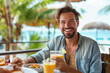 Cheerful young man having a hearty breakfast with fresh juice at a beachfront cafe