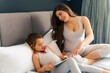 © DusanJelicic - Mom and daughter sitting on a bed and bounding before new baby arrives, watching cartoons on tablet placed on daughter's lap