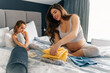 © DusanJelicic - A pregnant mom arranges things for the baby on the bed while her daughter sits next to her and looks sad