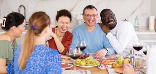 Wall Mural - Multicultural female and male friends chatting and drinking wine at table