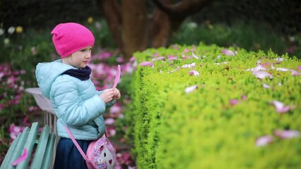 Wall Mural - Adorable preschooler girl enjoying pink magnolias in full bloom on a rainy day in a park of Paris, France.