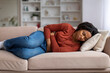 © Prostock-studio - Young black woman clutching her abdomen in discomfort at home