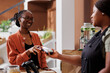 © DC Studio - An African American woman smiles, using her debit card to make a cashless payment for bio food items at a local market. Female seller accepting wireless transaction with a POS machine.